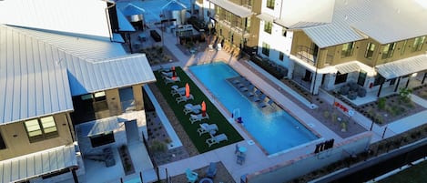 A modern building with a swimming pool, outdoor seating, and a fenced patio area.