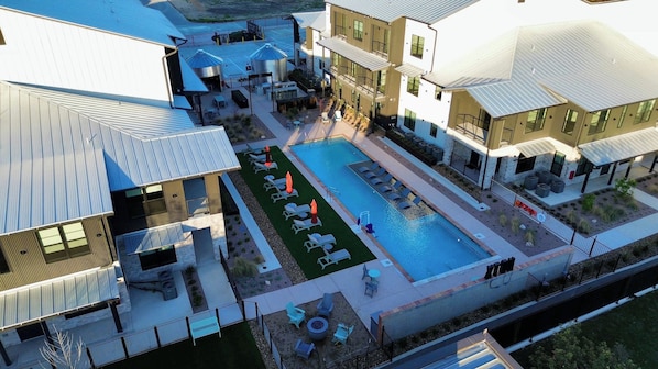 A modern building with a swimming pool, outdoor seating, and a fenced patio area. - Luxury Condo With Pool-view Balcony (New Braunfels)