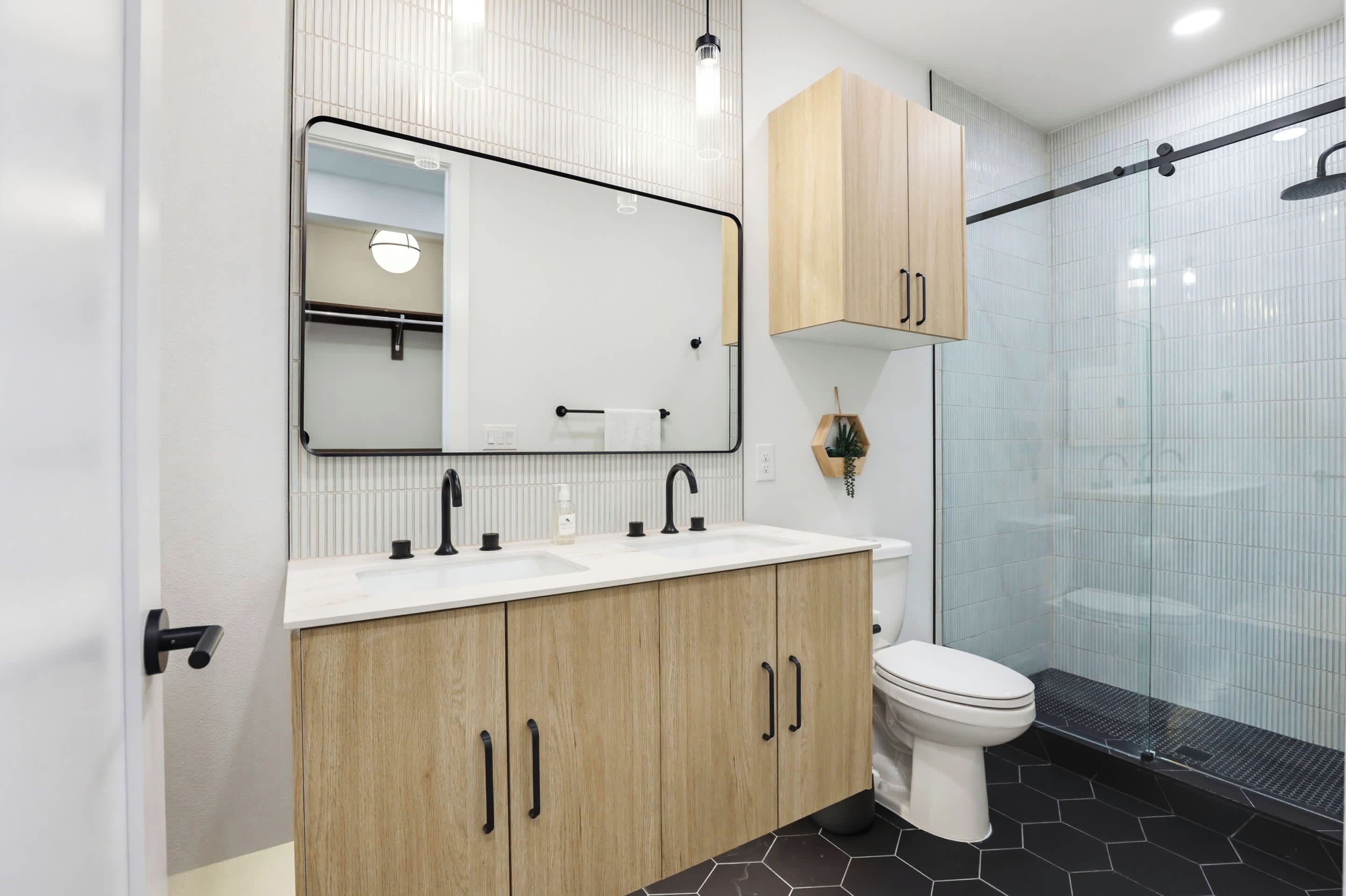 A modern bathroom with a white sink, wooden cabinets, a toilet, and a glass shower enclosure.