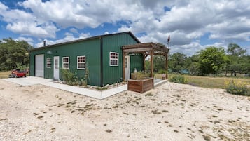 Ein grünes Gebäude mit Garage, einer Holzpergola und einem Schotterweg.
