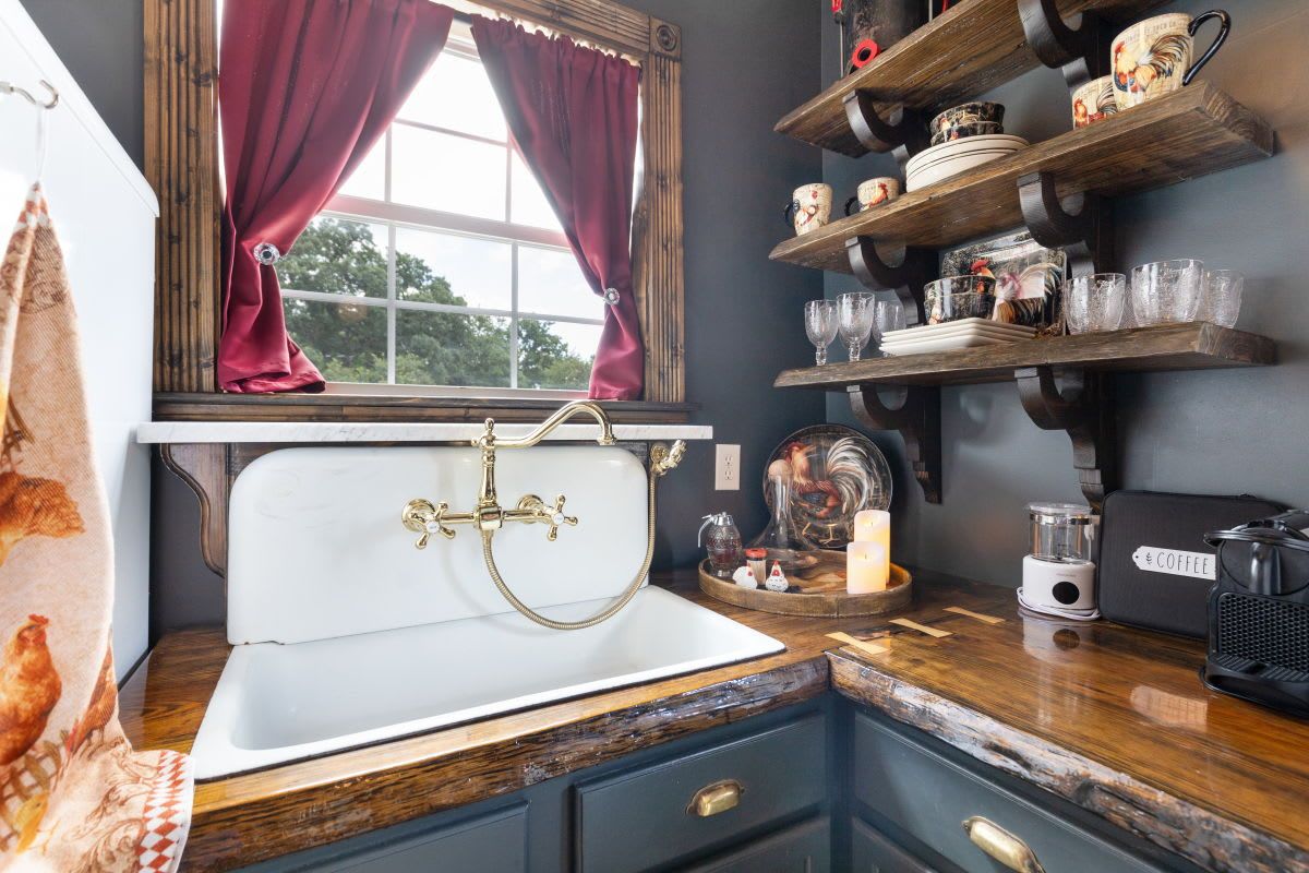 A vintage kitchen with a white sink, wooden shelves with dishes, and a coffee maker.