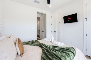 Quarto com cama, manta verde, decoração de cisne branco, televisão na parede e portas brancas.
