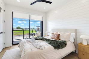 Quarto com cama, mesa de cabeceira, ventilador de teto e vista para uma paisagem verde através de uma porta de correr.