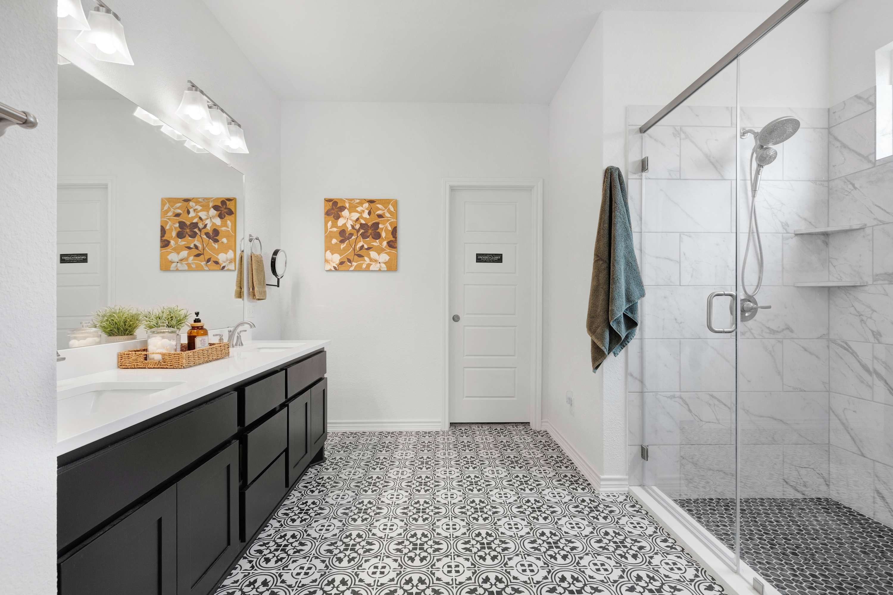 A modern bathroom with a white vanity, black cabinets, patterned floor tiles, and a glass-enclosed shower.