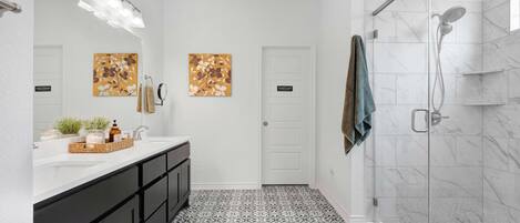 A modern bathroom with a white vanity, black cabinets, patterned floor tiles, and a glass-enclosed shower.