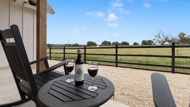 A table with two wine glasses and a bottle on a balcony with a view of a fenced field. - Birdsong Under the Stars Hot Tub, Fire Pit & Hill Country Views (Fredericksburg)