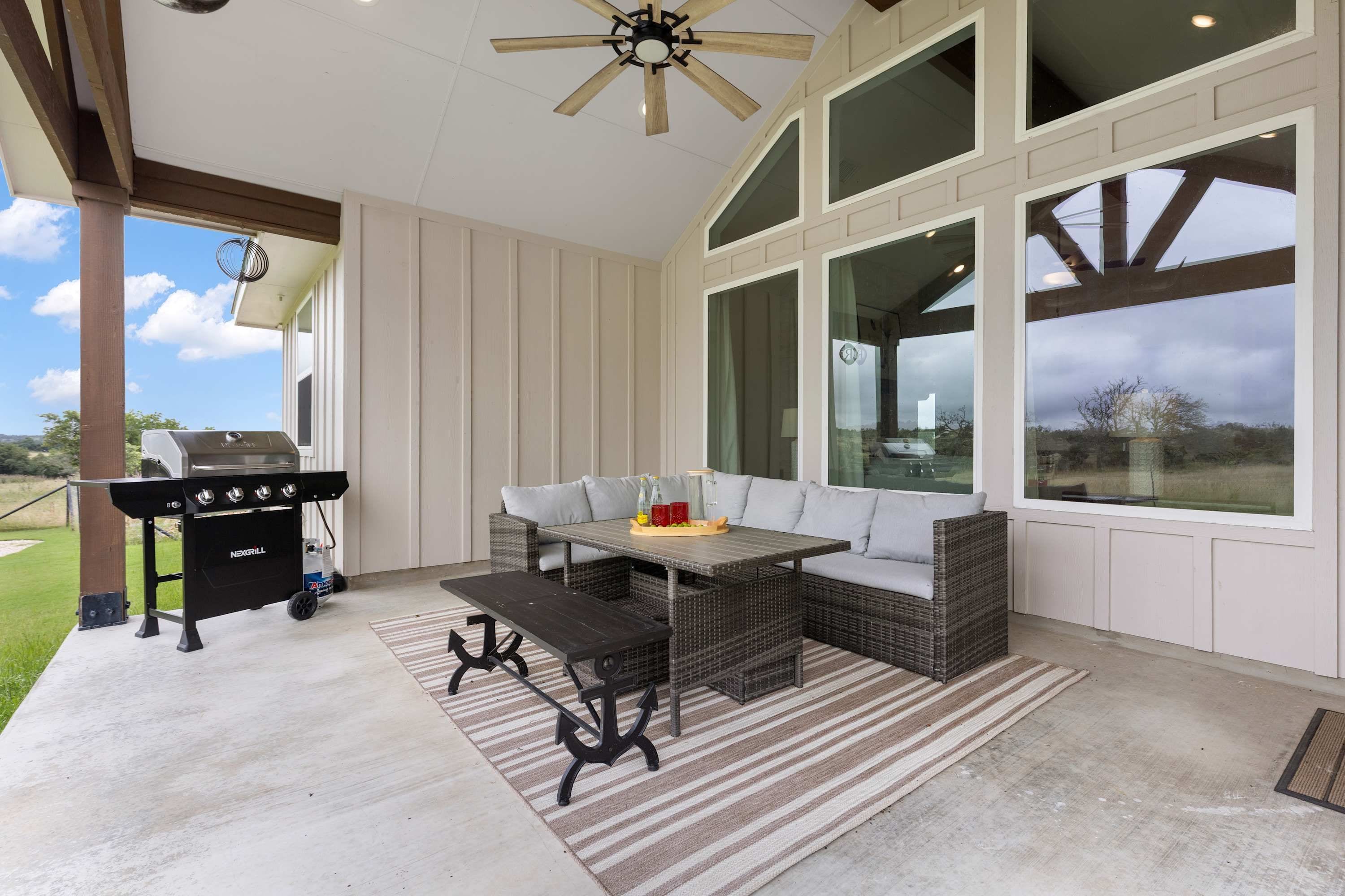 A covered patio area with a grill, outdoor furniture, and large windows.