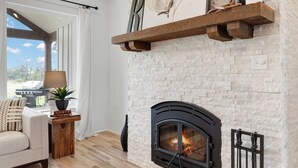 A living room with a fireplace, a sofa, a coffee table, and a view of the outdoors. - Birdsong Under the Stars Hot Tub, Fire Pit & Hill Country Views (Fredericksburg)