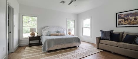 A bedroom with a bed, a ceiling fan, a sofa, and a painting on the wall.