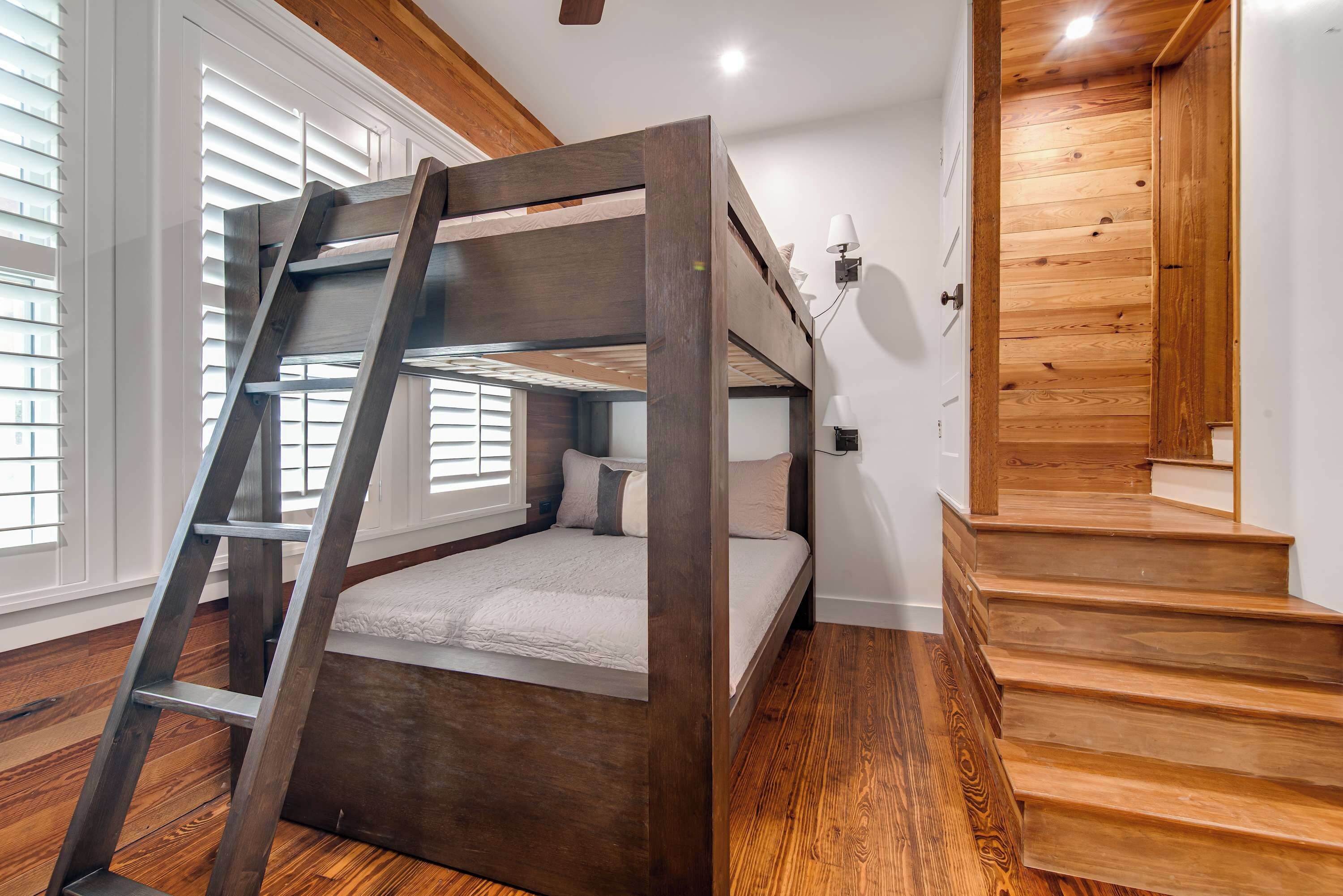 Una cama litera con escalera, piso de madera, una escalera y una ventana con persianas.
