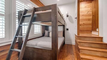 Una cama litera con escalera, piso de madera, una escalera y una ventana con persianas.
