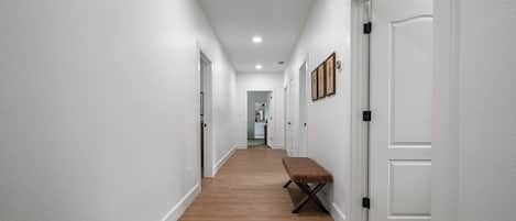 A hallway with white walls, wooden flooring, and a bench.