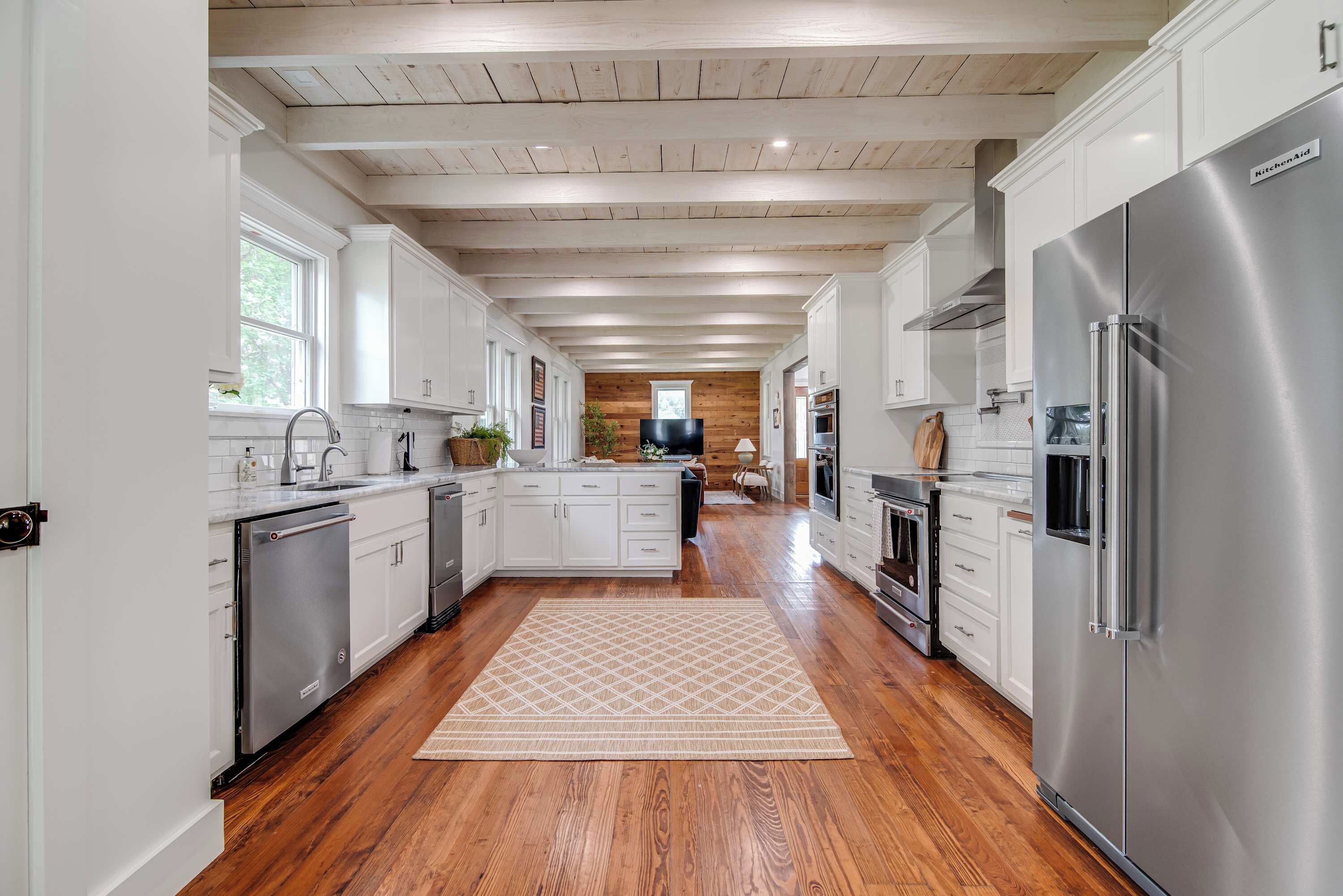 A spacious kitchen with wooden floors, white cabinets, stainless steel appliances, and a central island.