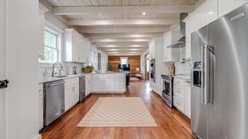 A spacious kitchen with wooden floors, white cabinets, stainless steel appliances, and a central island.