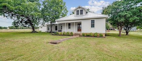A single-story house with a front porch, a small front yard, and a large tree to the left.