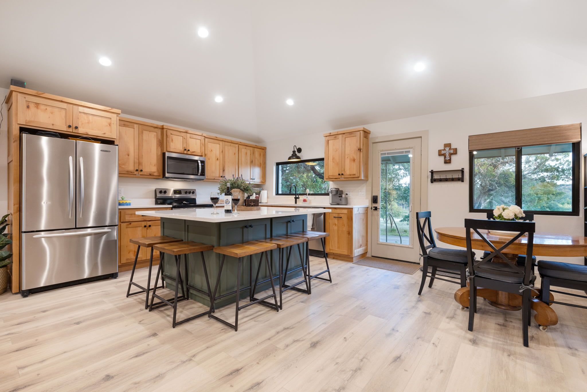 A modern kitchen with wooden cabinets, stainless steel appliances, a central island with bar stools, and a dining area with a wooden table and chairs.