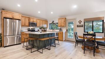 A modern kitchen with wooden cabinets, stainless steel appliances, a central island with bar stools, and a dining area with a wooden table and chairs.