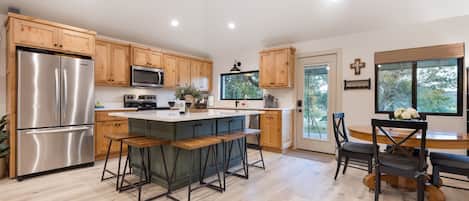 A modern kitchen with wooden cabinets, stainless steel appliances, a central island with bar stools, and a dining area with a wooden table and chairs.