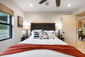 A bedroom with a large bed, two bedside lamps, a window with a view, and a door leading to another room. - Twisted Cedar Retreat (Ingram)