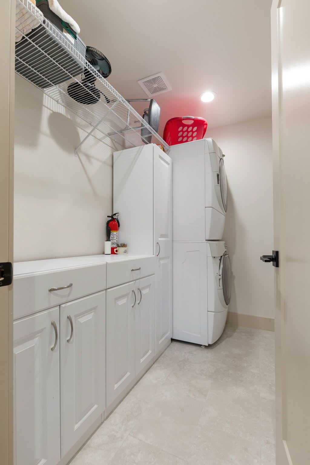 A compact kitchen with white cabinets, a white refrigerator, a red laundry basket, and a ceiling fan.