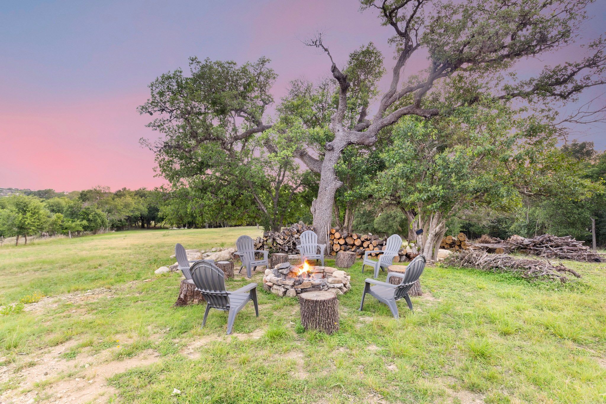 A fire pit surrounded by chairs in an outdoor setting with trees and a clear sky.