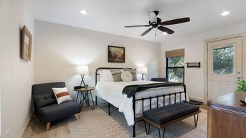 A bedroom with a bed, bedside tables, a chair, a bench, a ceiling fan, and a door with a window.