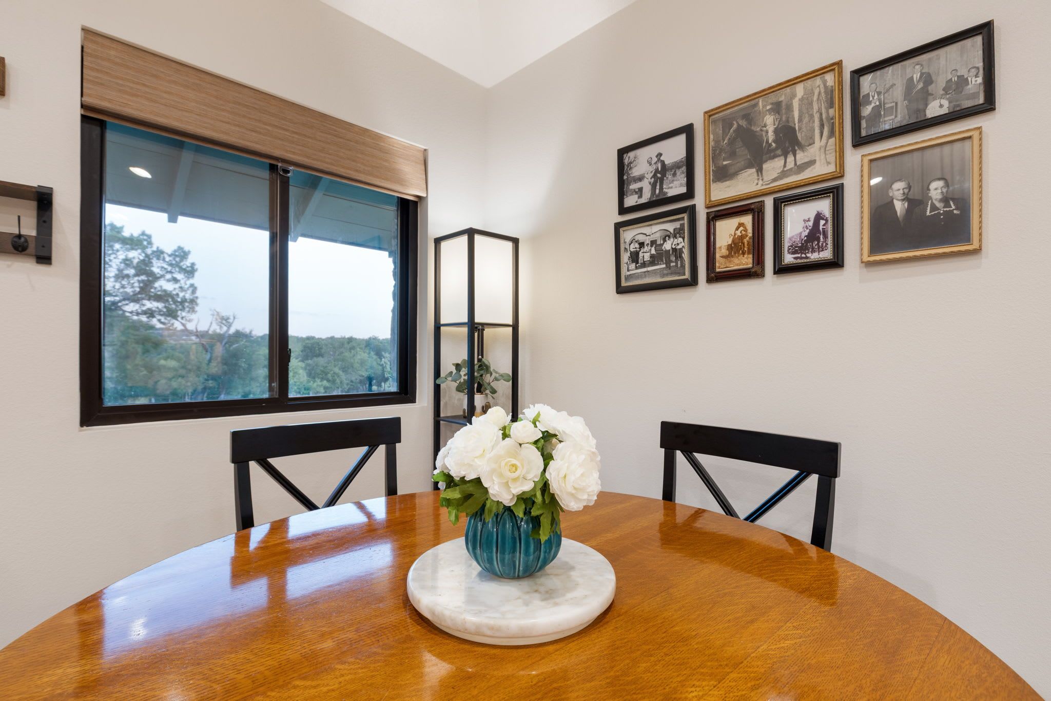 A dining table with a vase of white flowers, black chairs, and framed pictures on the wall.
