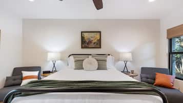 A hotel room with a large bed, two bedside tables, a ceiling fan, a painting on the wall, and a window with a view.