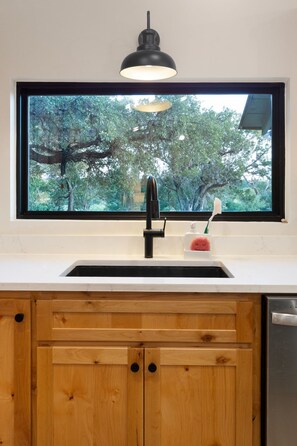 A kitchen with a large window, a black faucet, and a wooden cabinet.