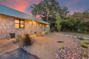 A stone building with a metal roof, a gravel driveway, and a large tree in the background. - Twisted Cedar Retreat (Ingram)