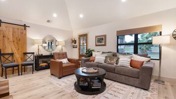 A living room with a sofa, armchairs, a coffee table, a wooden sliding door, a mirror, and a large window.