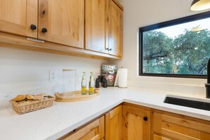Una cocina con armarios de madera, una ventana con vistas a árboles, una encimera con alimentos y un lavabo.
