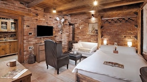 A cozy room with exposed brick walls, a wooden ceiling, a flat-screen TV, a sofa, a bed, and a small table with a mug. - Cozy little house near Zagreb and airport. Private garden around house. (Dugo Selo)