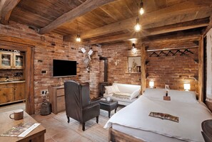 Una habitación acogedora con paredes de ladrillo visto, techo de madera, televisor de pantalla plana, un sofá, una cama y una mesita con una taza.