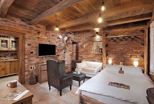 Una habitación acogedora con paredes de ladrillo visto, techo de madera, televisor de pantalla plana, un sofá, una cama y una mesita con una taza.