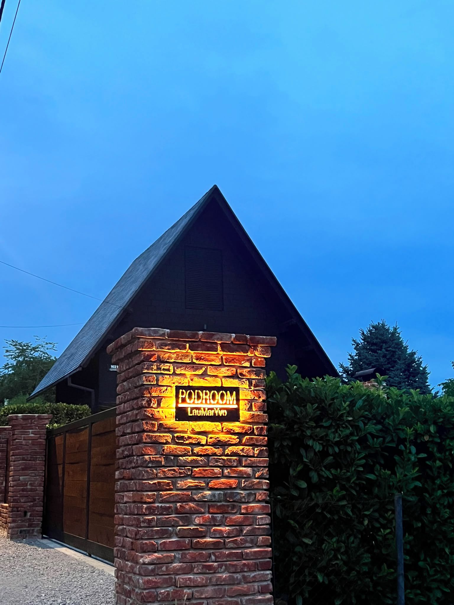 A brick wall with a neon sign for 'Podroom LauMarYvo' against a clear blue sky.
