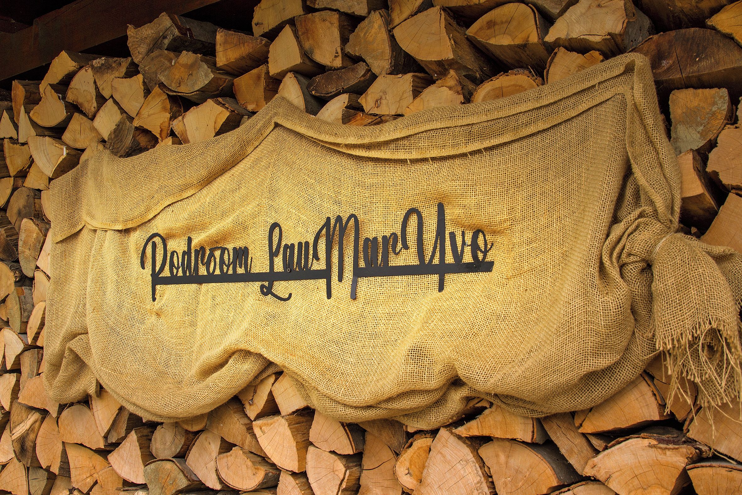 A burlap sack with the text 'Podroom' on it, surrounded by stacked firewood.