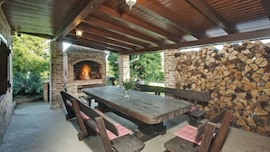 An outdoor patio with a brick fireplace, wooden benches, and a table. - Cozy little house near Zagreb and airport. Private garden around house. (Dugo Selo)