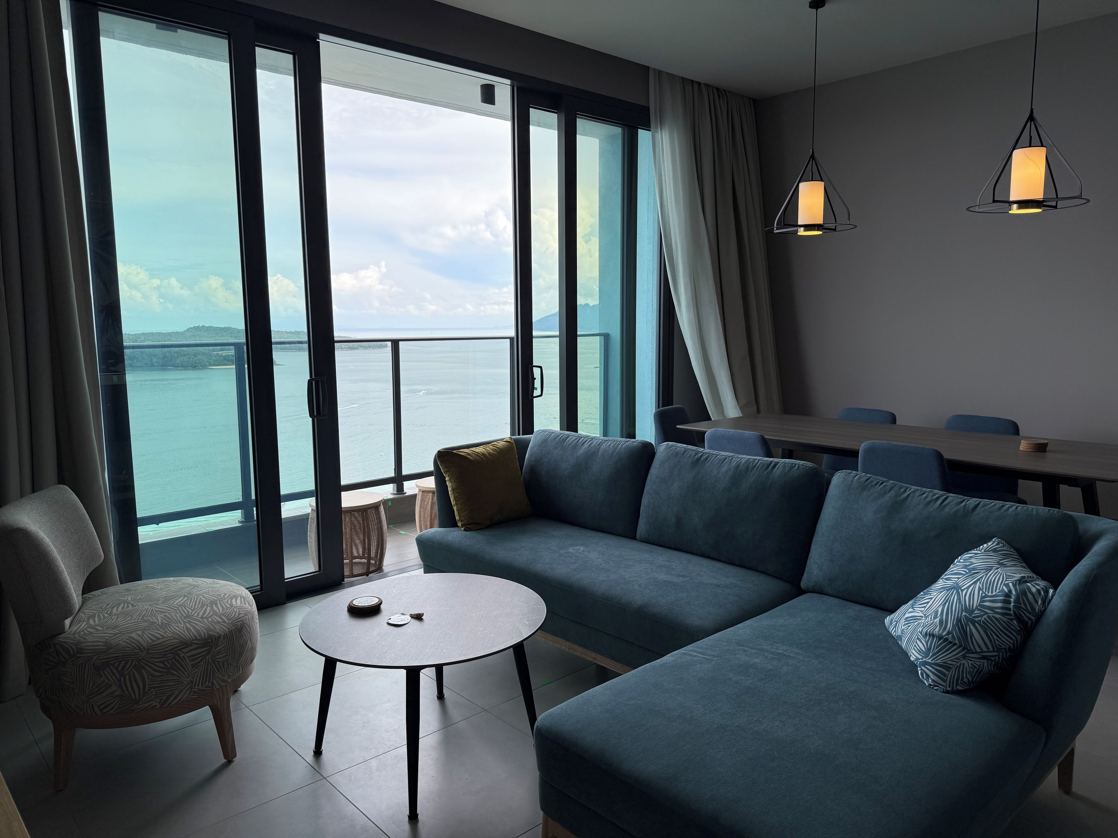 Ein modernes Wohnzimmer mit einer Couch, einem kleinen runden Tisch und Meerblick durch große Fenster.