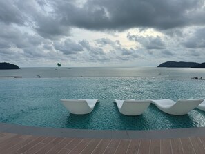 A swimming pool with lounge chairs, a view of the sea, and distant islands. - Seafront - Spacious 4-bedroom apartment in charming Langkawi with AC (Langkawi)