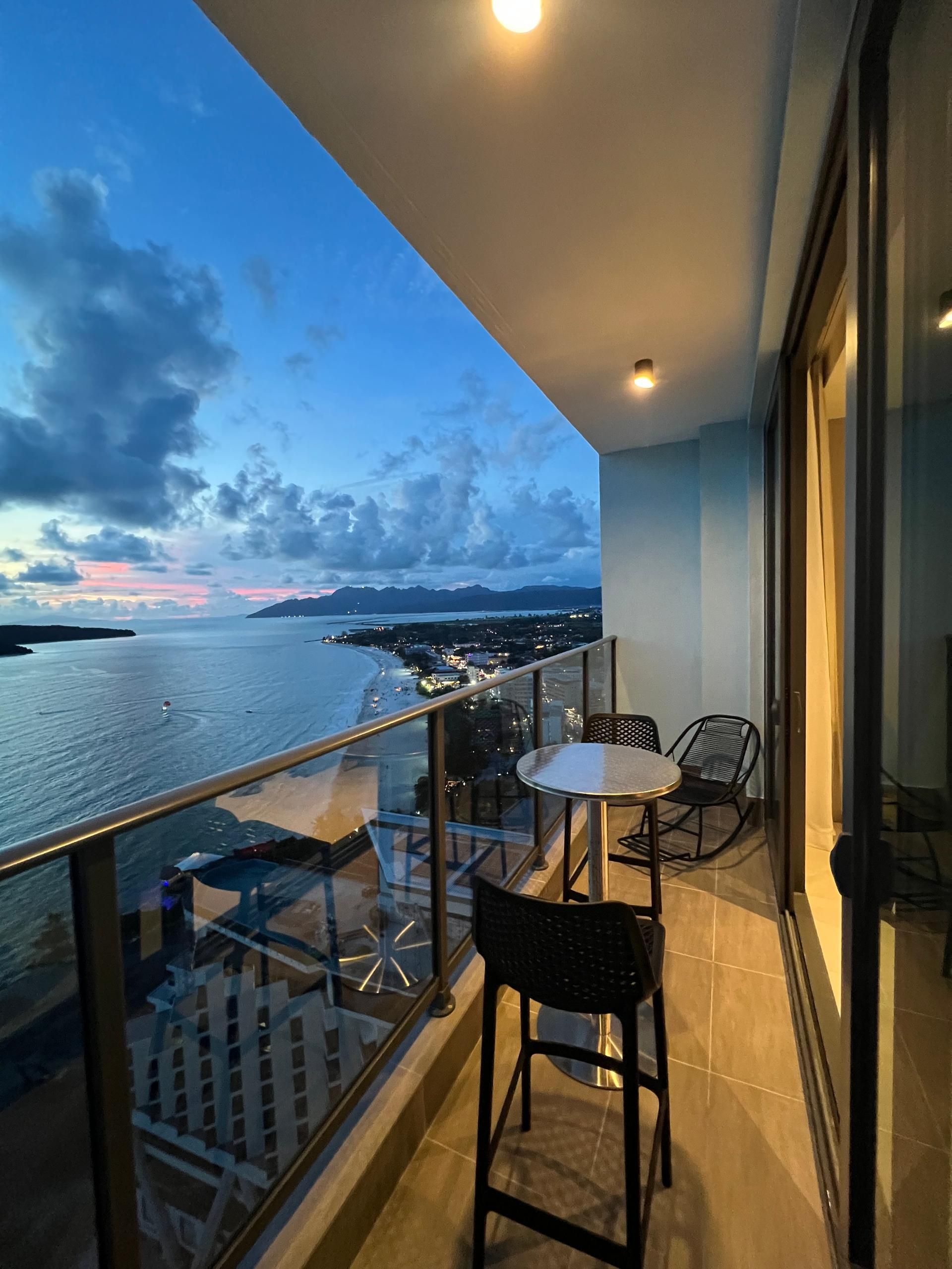 A balcony with a table and chairs, overlooking a beach and cityscape.