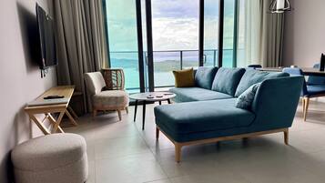 A modern living room with a sofa, ottoman, and a table with a laptop.