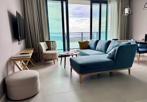 A modern living room with a sofa, ottoman, and a table with a laptop.