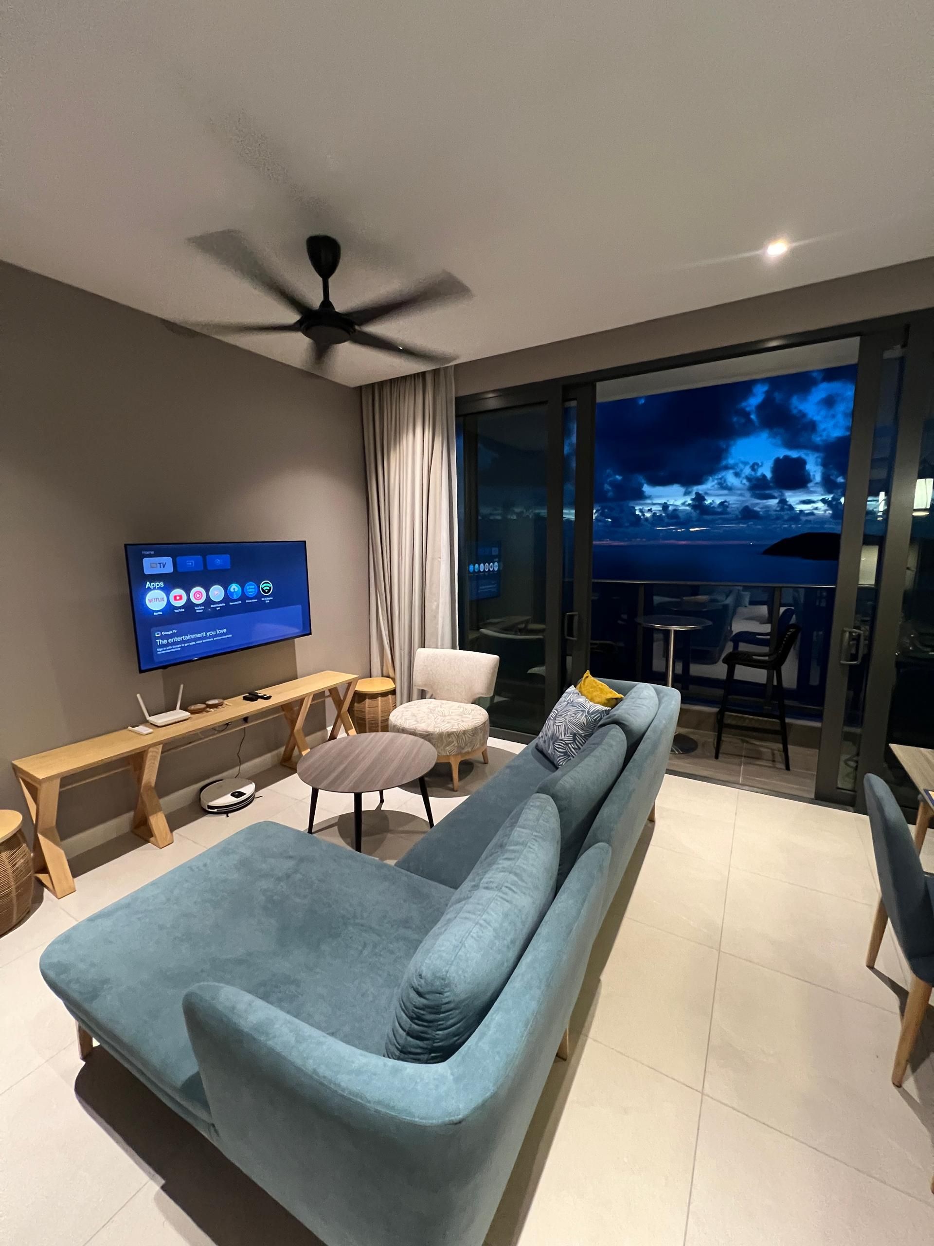 A modern living room with a sofa, a TV, a ceiling fan, and a view of the outdoors.