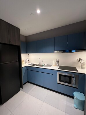 A modern kitchen with blue cabinets, a stainless steel refrigerator, a sink, and a built-in microwave.