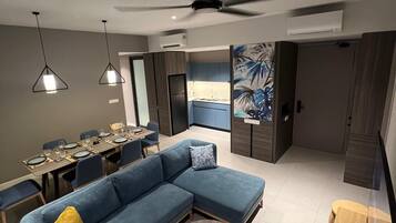 A modern living room with a sectional sofa, a dining table set for six, a ceiling fan, and an air conditioning unit.