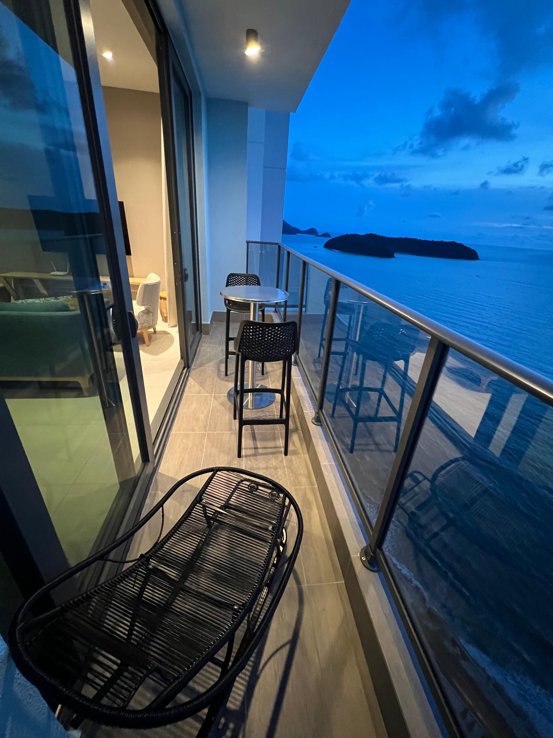 A balcony with a table and chairs, a view of the sea, and a glass door leading into the room.