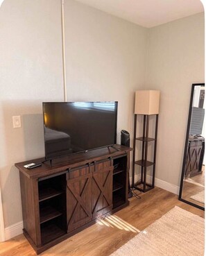 A living room with a TV on a wooden entertainment center, a standing lamp, and a mirror reflecting part of the room. - Beautiful condo in fabulous Pompano Beach across from the beach! (Pompano Beach)
