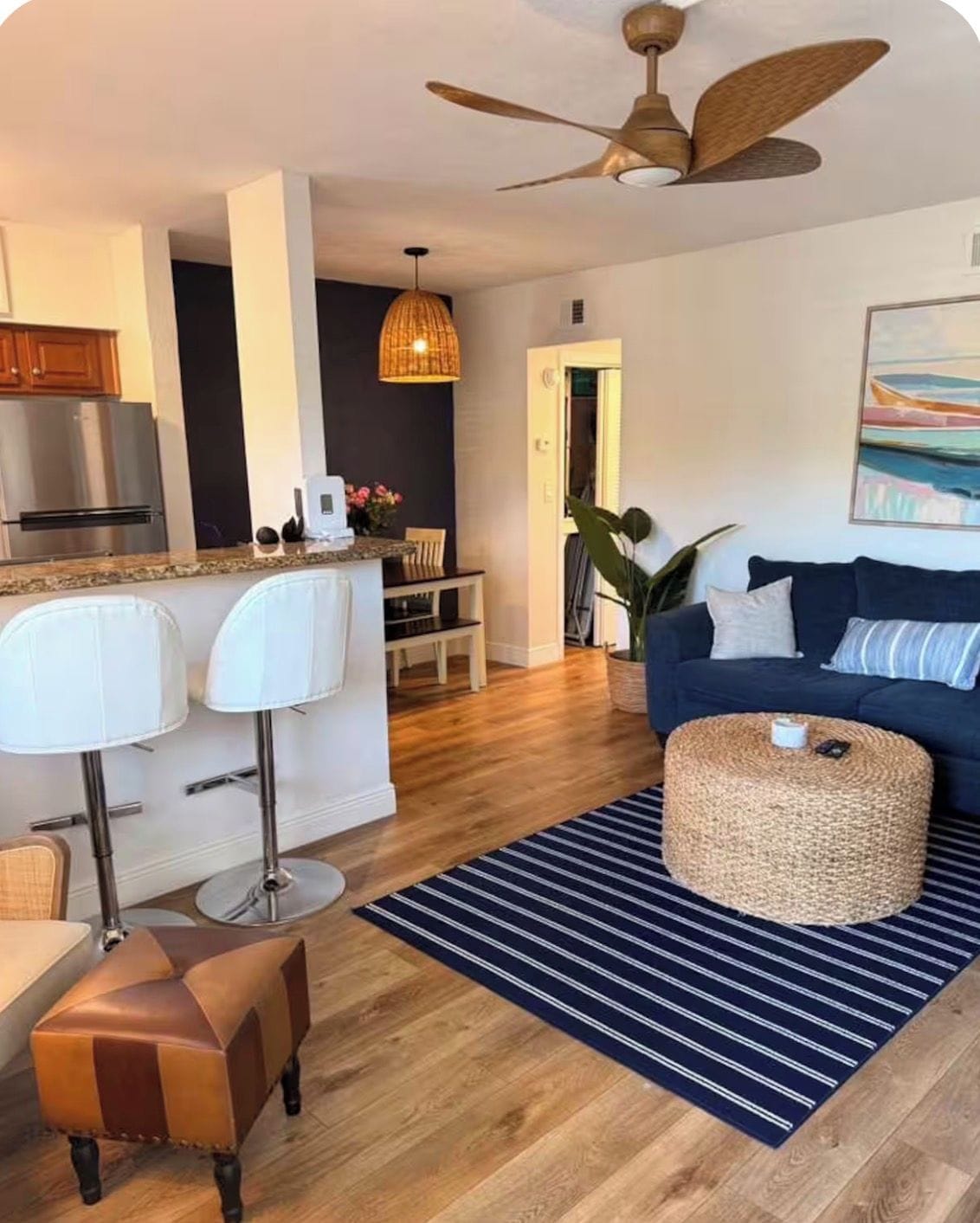 A modern living room with a blue sofa, a woven ottoman, and a striped rug.