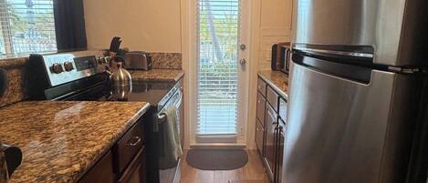 A compact kitchen with a stainless steel refrigerator, a gas stove, and wooden cabinets.